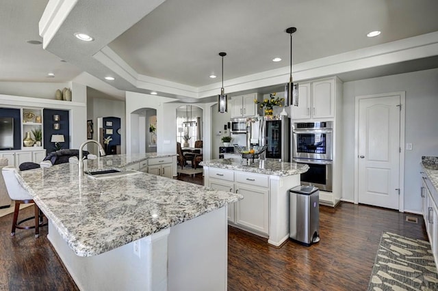 10919 Cascading Spring Cir, Peyton, CO 80831 - kitchen featuring a sink, a spacious island, arched walkways, appliances with stainless steel finishes, and dark wood-style floors