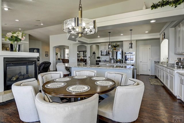10919 Cascading Spring Cir, Peyton, CO 80831 - dining space with arched walkways, a chandelier, dark wood-type flooring, recessed lighting, and a multi sided fireplace