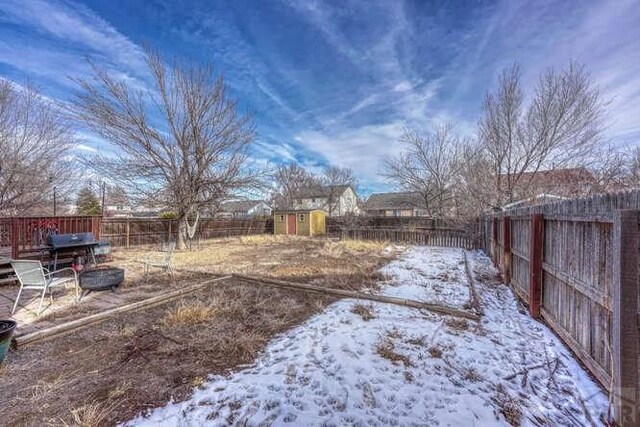 yard covered in snow with a storage shed, a fenced backyard, and an outbuilding