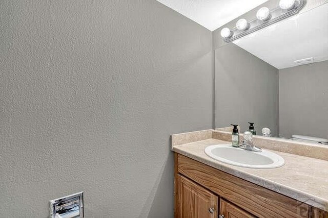 half bath featuring toilet, a textured wall, and vanity