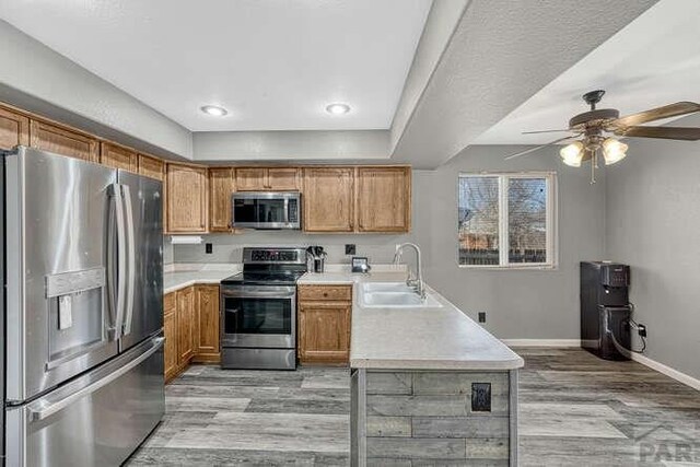 kitchen with light countertops, appliances with stainless steel finishes, brown cabinetry, a sink, and light wood-type flooring