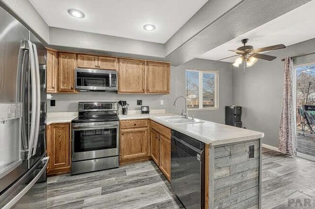 kitchen featuring stainless steel appliances, brown cabinetry, light countertops, and a peninsula