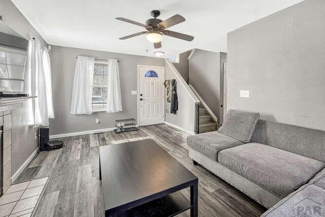 living area featuring a ceiling fan, stairs, baseboards, and wood finished floors