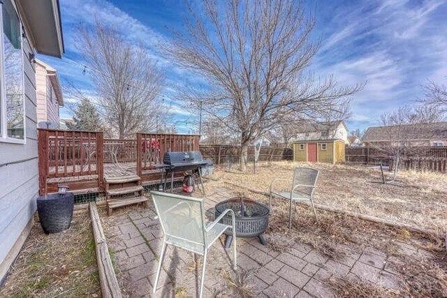 view of patio with an outbuilding, a storage shed, a deck, a fenced backyard, and a fire pit