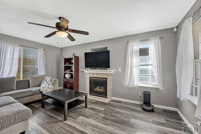 living area featuring ceiling fan, a fireplace, baseboards, and wood finished floors