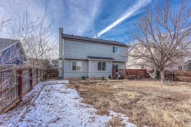 snow covered rear of property with a fenced backyard and a chimney