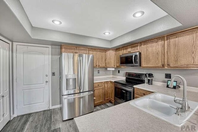 kitchen with appliances with stainless steel finishes, light countertops, a sink, and wood finished floors