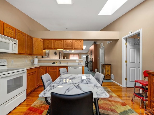 kitchen with light countertops, visible vents, vaulted ceiling, a sink, and white appliances