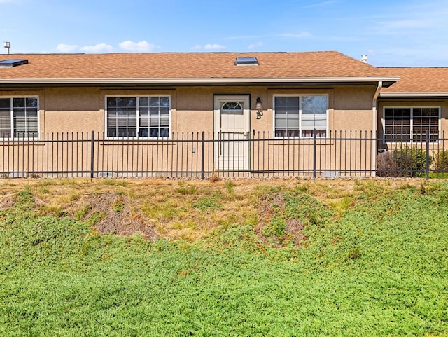 ranch-style house featuring a shingled roof, fence, and stucco siding