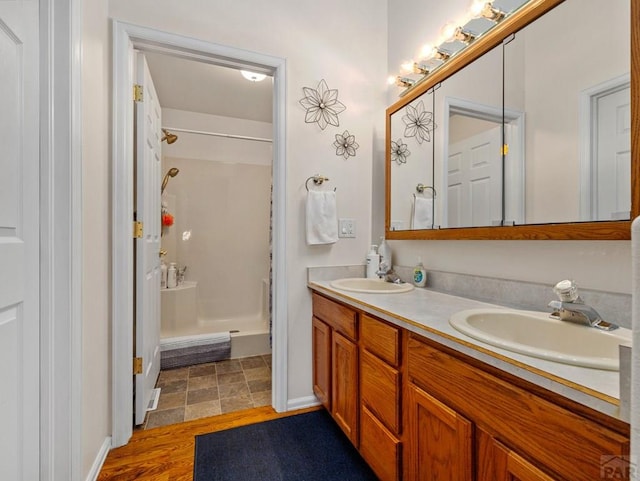 bathroom featuring double vanity, a shower, a sink, and wood finished floors