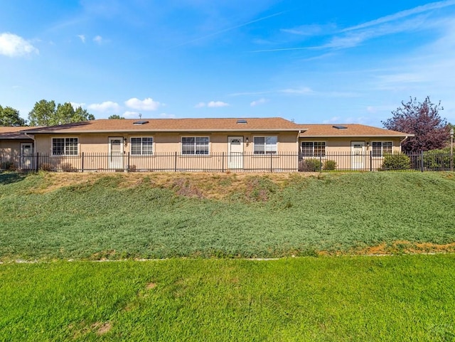 rear view of house featuring a yard, fence, and stucco siding