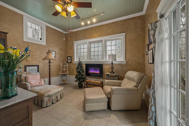 sitting room featuring a ceiling fan, light tile patterned flooring, track lighting, a glass covered fireplace, and crown molding