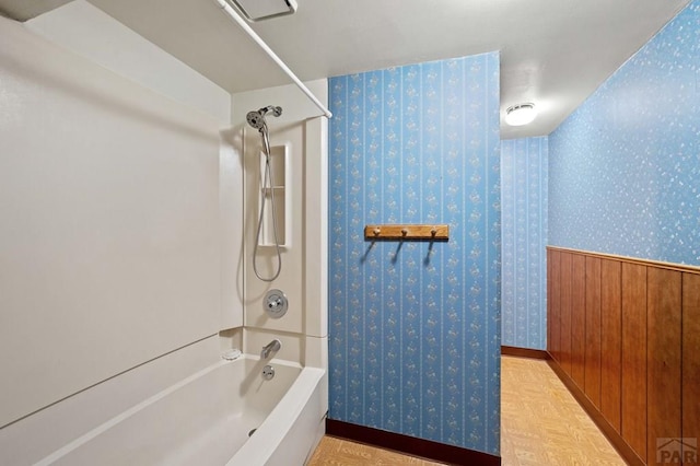 bathroom with wallpapered walls, tub / shower combination, and a wainscoted wall