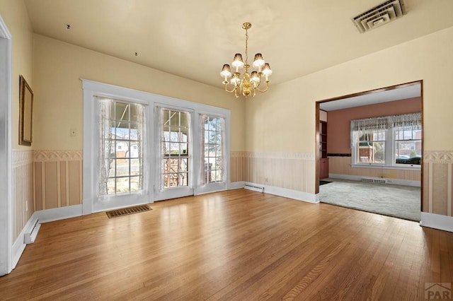 unfurnished dining area with visible vents, wood finished floors, a wainscoted wall, and a chandelier