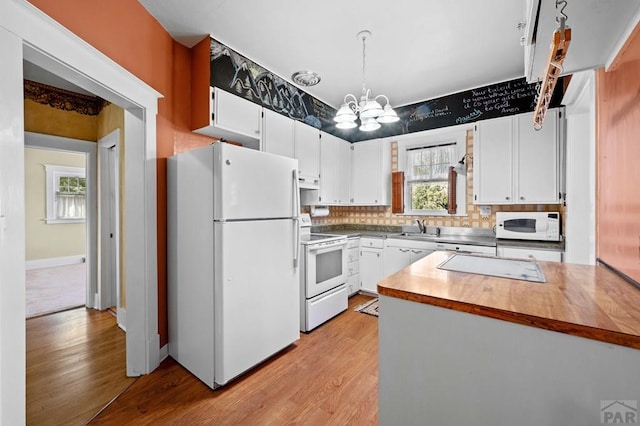 kitchen featuring white appliances, light wood-style flooring, a sink, under cabinet range hood, and a chandelier