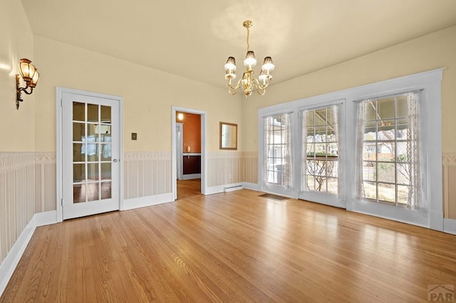 unfurnished dining area featuring light wood-style floors, visible vents, a chandelier, and wainscoting