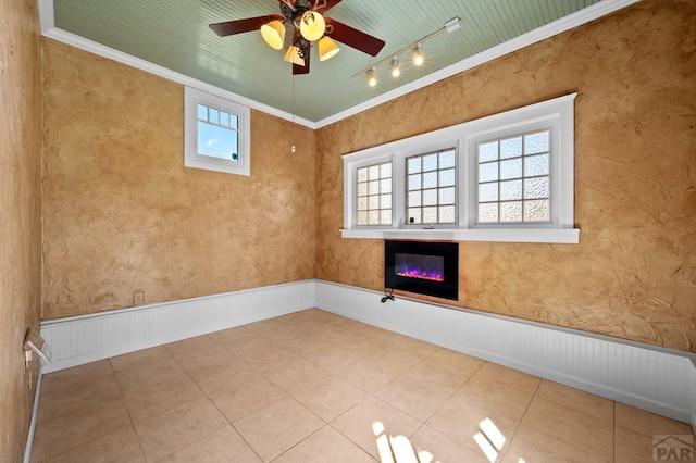 unfurnished room with tile patterned floors, ornamental molding, track lighting, a glass covered fireplace, and wainscoting