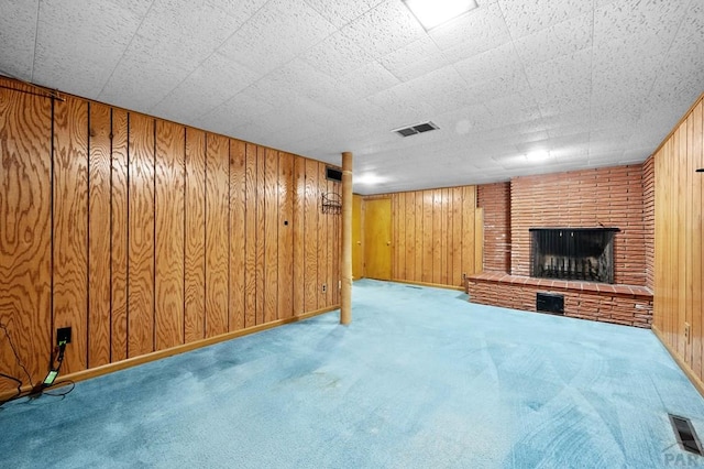 finished basement with visible vents, carpet flooring, a brick fireplace, and wooden walls