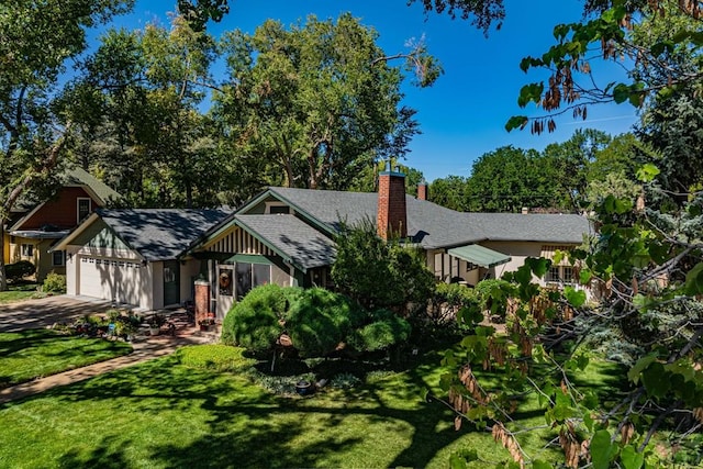 view of front of house featuring roof with shingles, a front yard, a chimney, a garage, and driveway