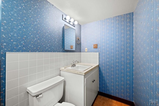 half bathroom featuring toilet, vanity, and wallpapered walls