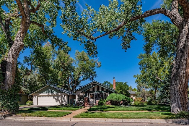 view of front facade with a chimney, an attached garage, concrete driveway, and a front yard