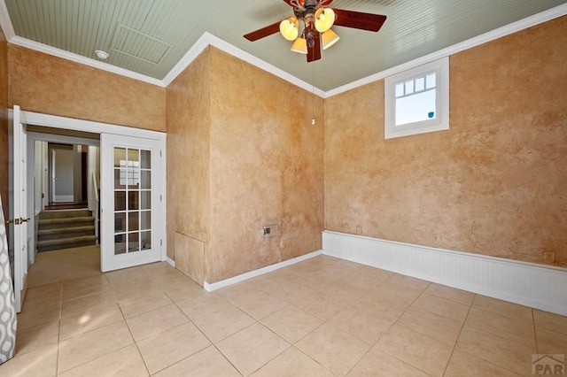 spare room featuring stairway, light tile patterned flooring, wainscoting, crown molding, and ceiling fan