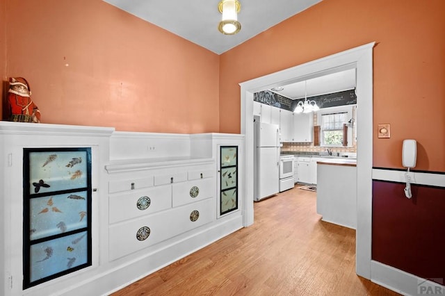 interior space with light wood-type flooring, light countertops, freestanding refrigerator, stove, and white cabinets