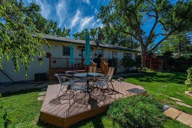 back of property with a deck, outdoor dining area, a lawn, and stucco siding