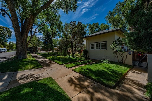 view of side of property featuring a gate, a lawn, and stucco siding