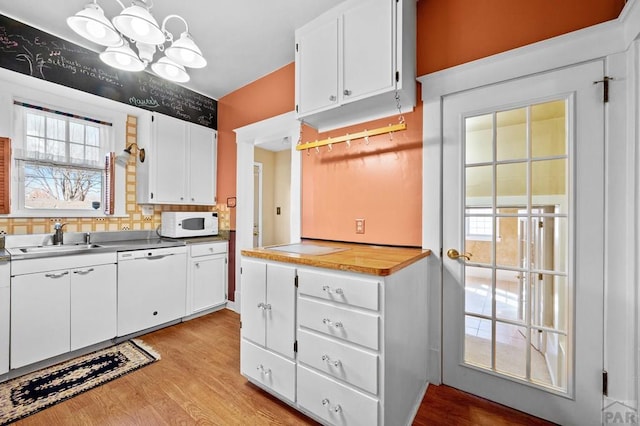 kitchen featuring white appliances, white cabinets, light wood-style floors, and a sink