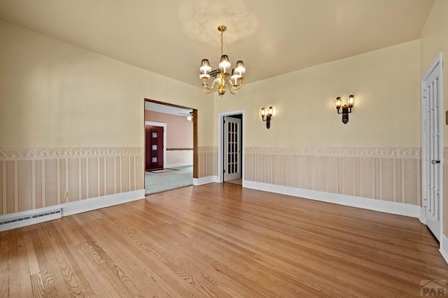 unfurnished room featuring light wood-style flooring, a baseboard heating unit, wainscoting, baseboards, and a chandelier