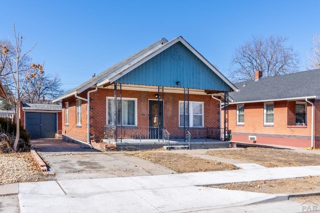 bungalow featuring covered porch, driveway, brick siding, and an outdoor structure