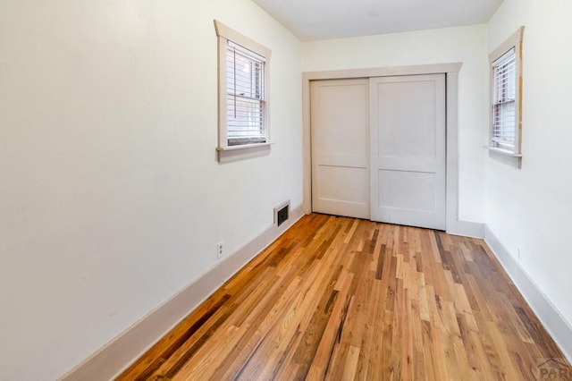 unfurnished bedroom with light wood-type flooring, baseboards, visible vents, and a closet