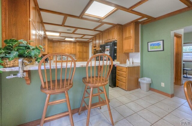 kitchen featuring brown cabinetry, freestanding refrigerator, light countertops, and a kitchen bar