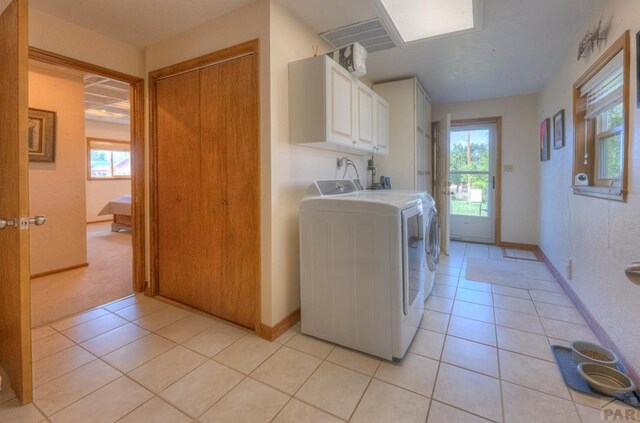 laundry room featuring a healthy amount of sunlight, cabinet space, washing machine and dryer, and light tile patterned floors