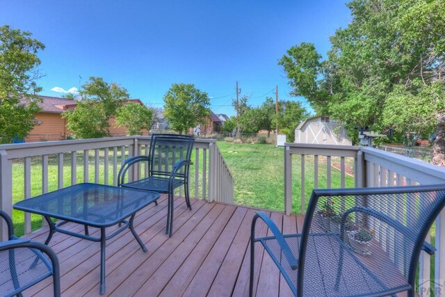 wooden deck with a shed, a fenced backyard, a lawn, and an outbuilding