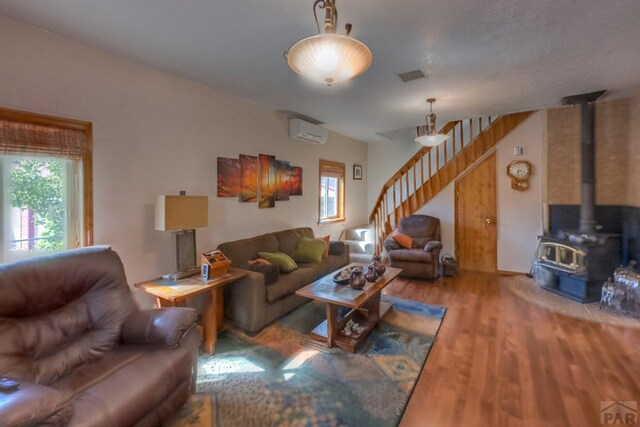 living area with visible vents, wood finished floors, a wood stove, stairs, and an AC wall unit