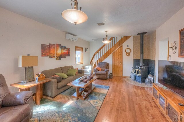 living area featuring a wall unit AC, visible vents, light wood-style floors, stairway, and a wood stove