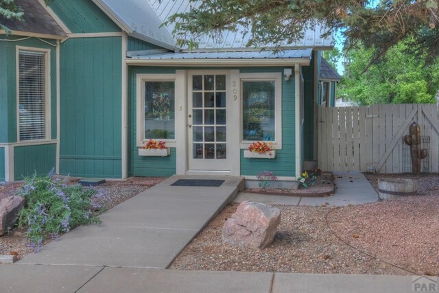 entrance to property featuring board and batten siding, metal roof, and fence