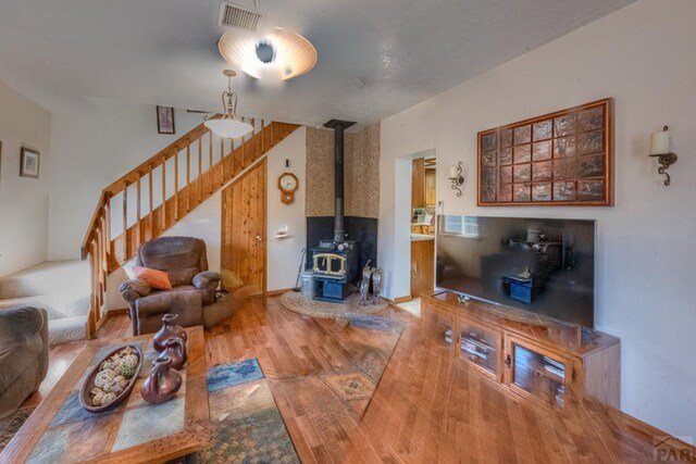 living room with baseboards, visible vents, stairway, wood finished floors, and a wood stove