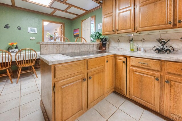 kitchen with light tile patterned flooring, black electric cooktop, a peninsula, backsplash, and brown cabinetry