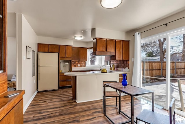 kitchen featuring backsplash, brown cabinets, a peninsula, freestanding refrigerator, and dark wood-style flooring