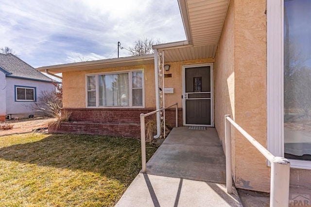 view of exterior entry featuring a lawn and stucco siding