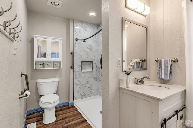 bathroom with vanity, wood finished floors, baseboards, a tile shower, and toilet