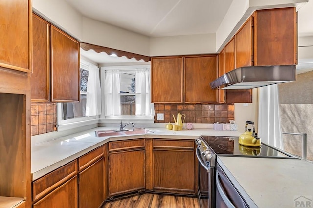 kitchen with stainless steel electric range, a sink, light countertops, under cabinet range hood, and tasteful backsplash