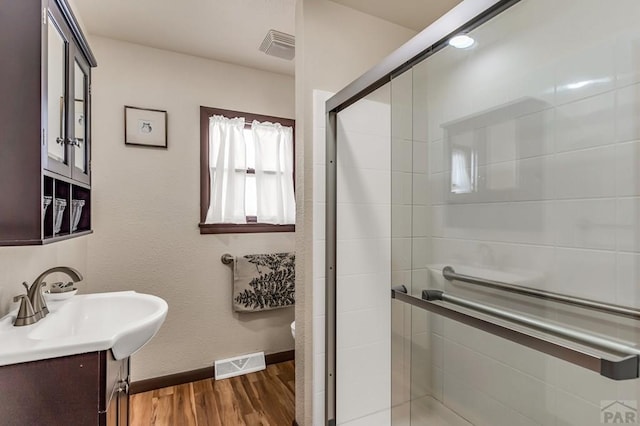 full bath with vanity, wood finished floors, baseboards, visible vents, and a stall shower