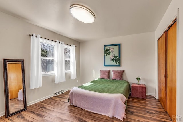 bedroom with wood finished floors, visible vents, a closet, and baseboards