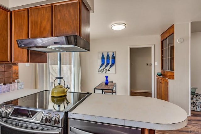 kitchen featuring under cabinet range hood, stainless steel electric range oven, light countertops, decorative backsplash, and brown cabinets