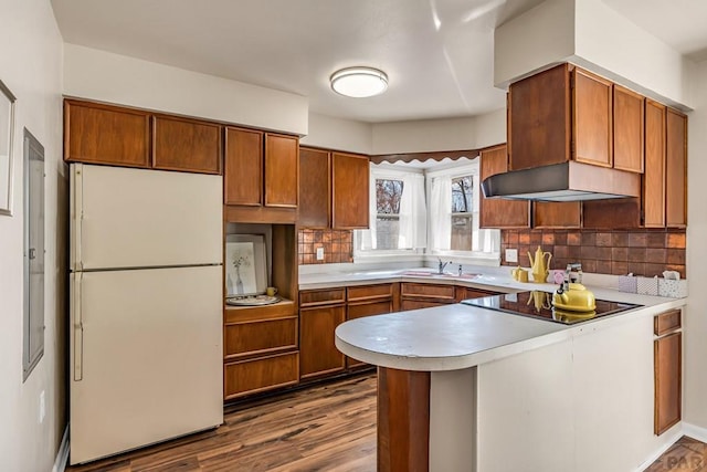 kitchen with black electric stovetop, light countertops, a peninsula, freestanding refrigerator, and a sink