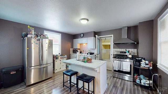 kitchen featuring light countertops, wall chimney exhaust hood, wood finished floors, and stainless steel appliances